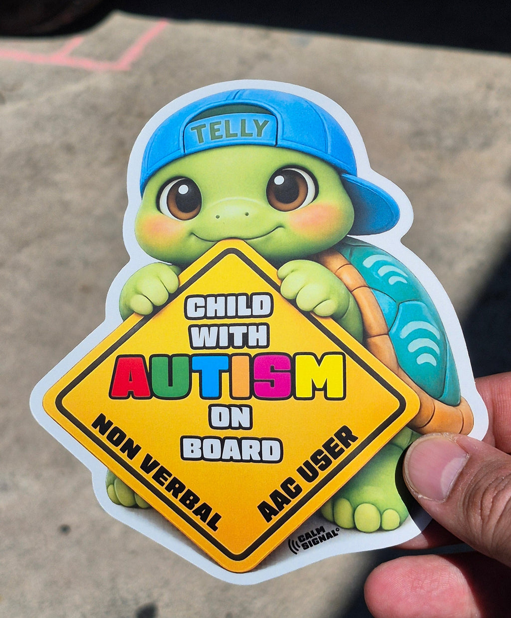 Sticker of a turtle with autism awareness text held by a hand on a concrete surface.