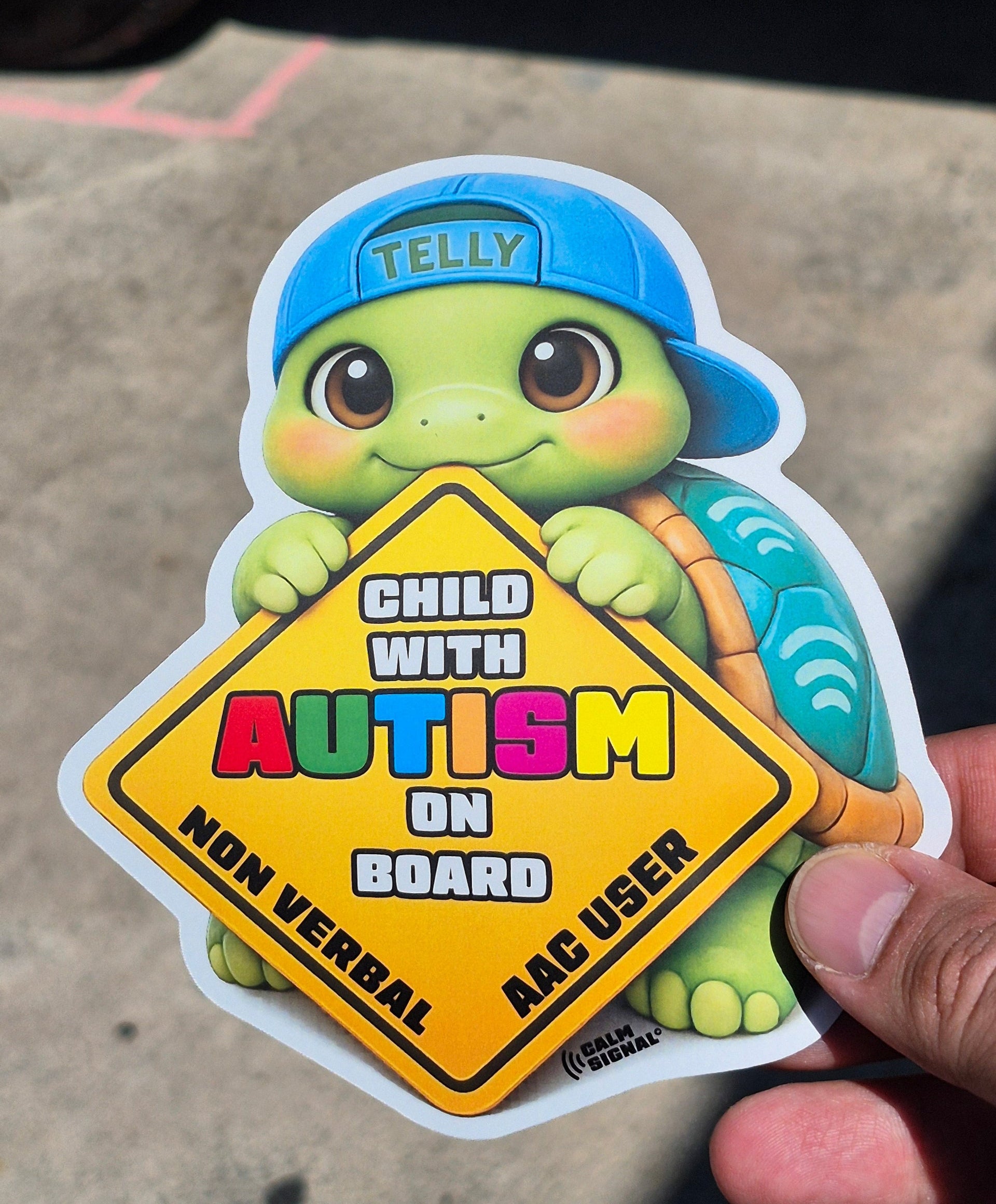 Sticker of a turtle with autism awareness text held by a hand on a concrete surface.